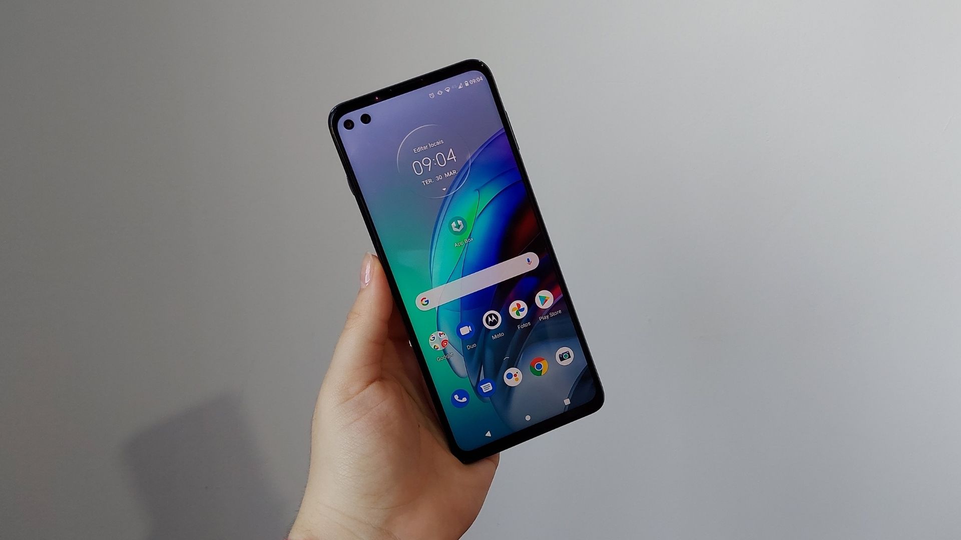 Mão segurando Moto G100 e exibindo parte frontal do celular