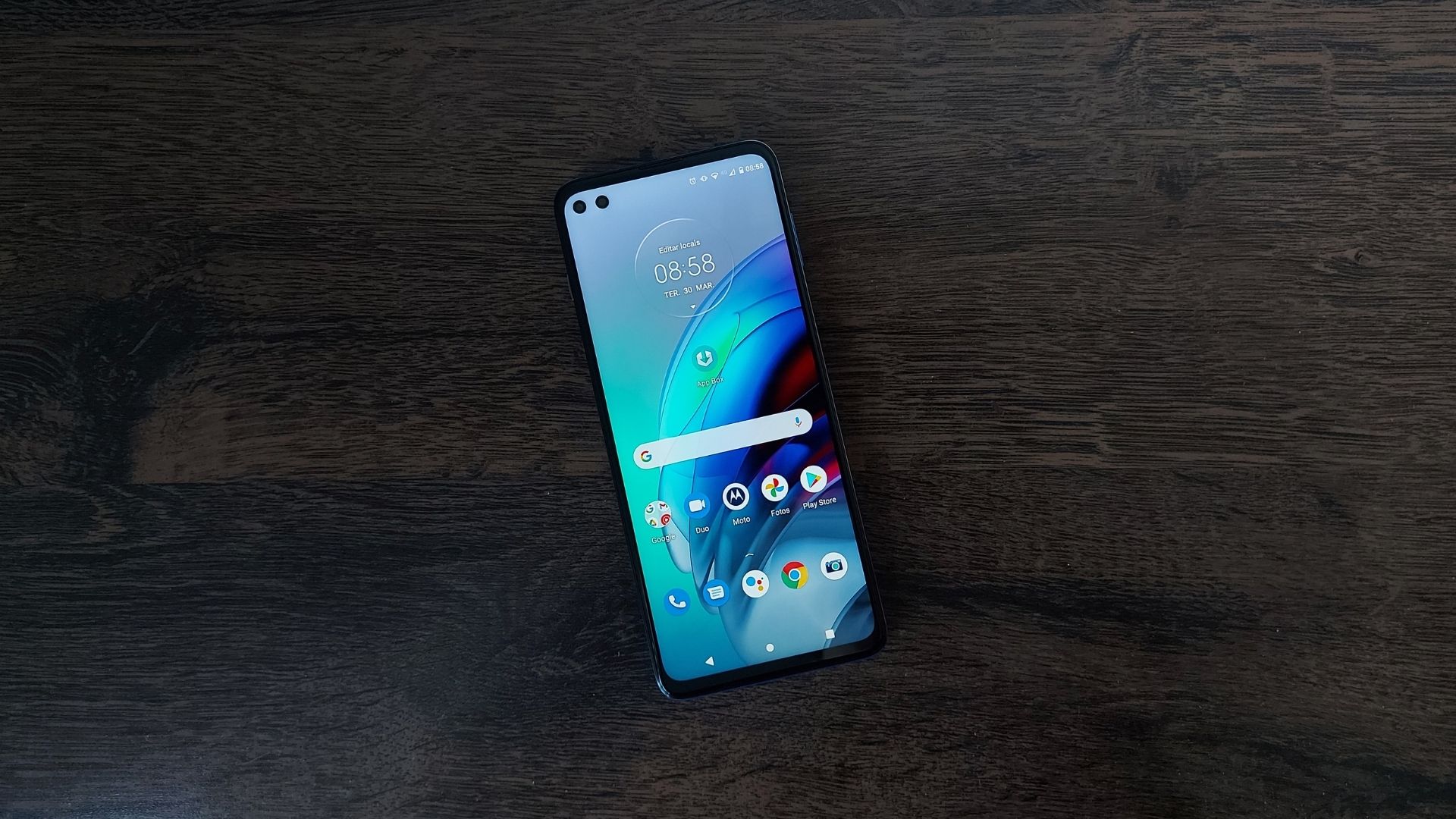 Moto G100 em cima de ums mesa de madeira e com parte frontal virada para cima