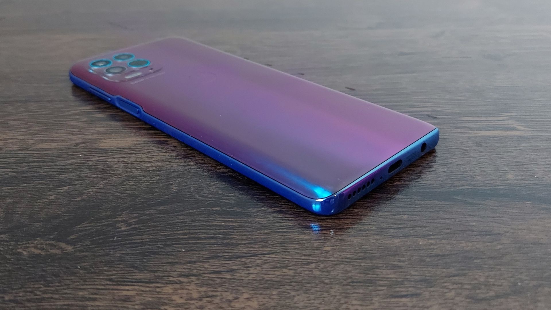 Moto G100 em cima de uma mesa de madeira e com parte traseira virada para cima e ângulo diferente