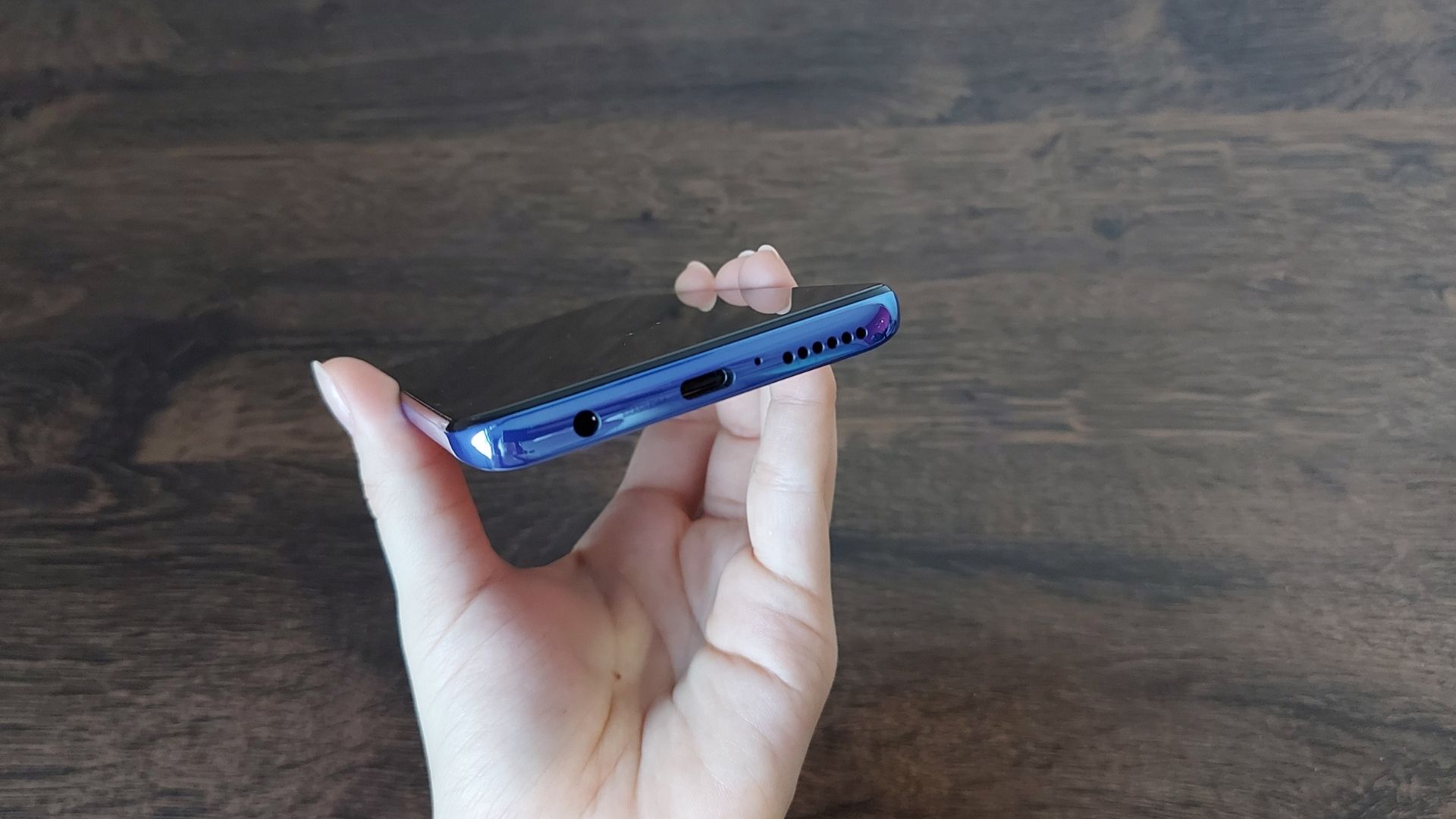 Mão mostrando parte de baixo do Moto G100, com mesa de madeira no fundo