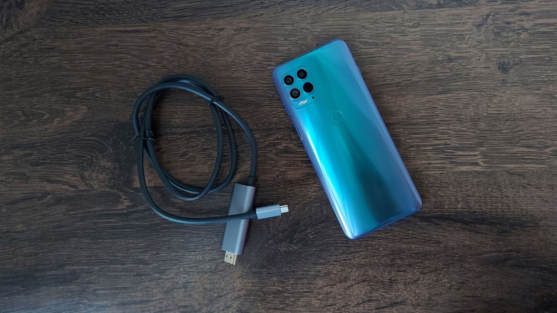 Foto do Moto G100 copm parte traseira virada para cima e cabo carregador ao lado