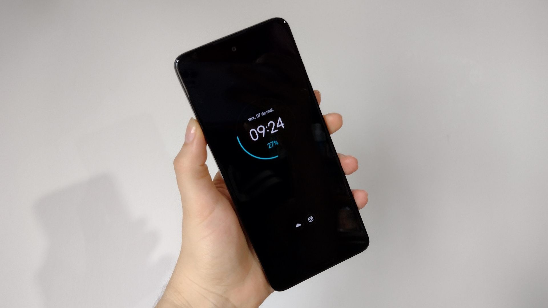 Mão segurando Moto G60 e exibindo a parte frontal do celular, com uma parede ao fundo